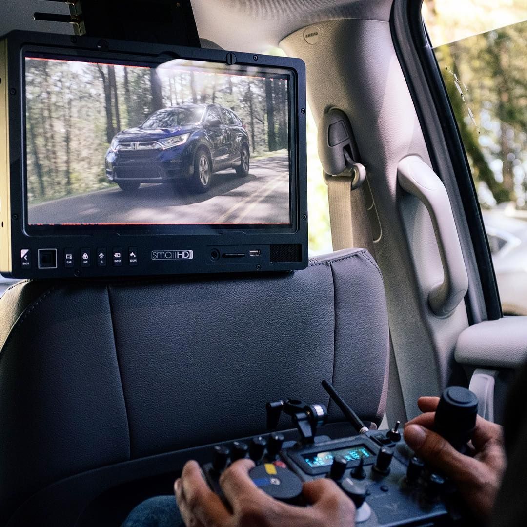 SmallHD monitor gripped to a minivan headrest showing the Honda CR-V driving shot through the woods, MotoCrane controller in hand