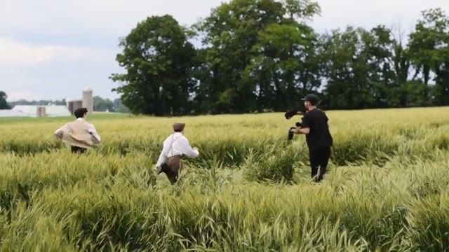 operator running through the wheat field behind two period-dressed kids